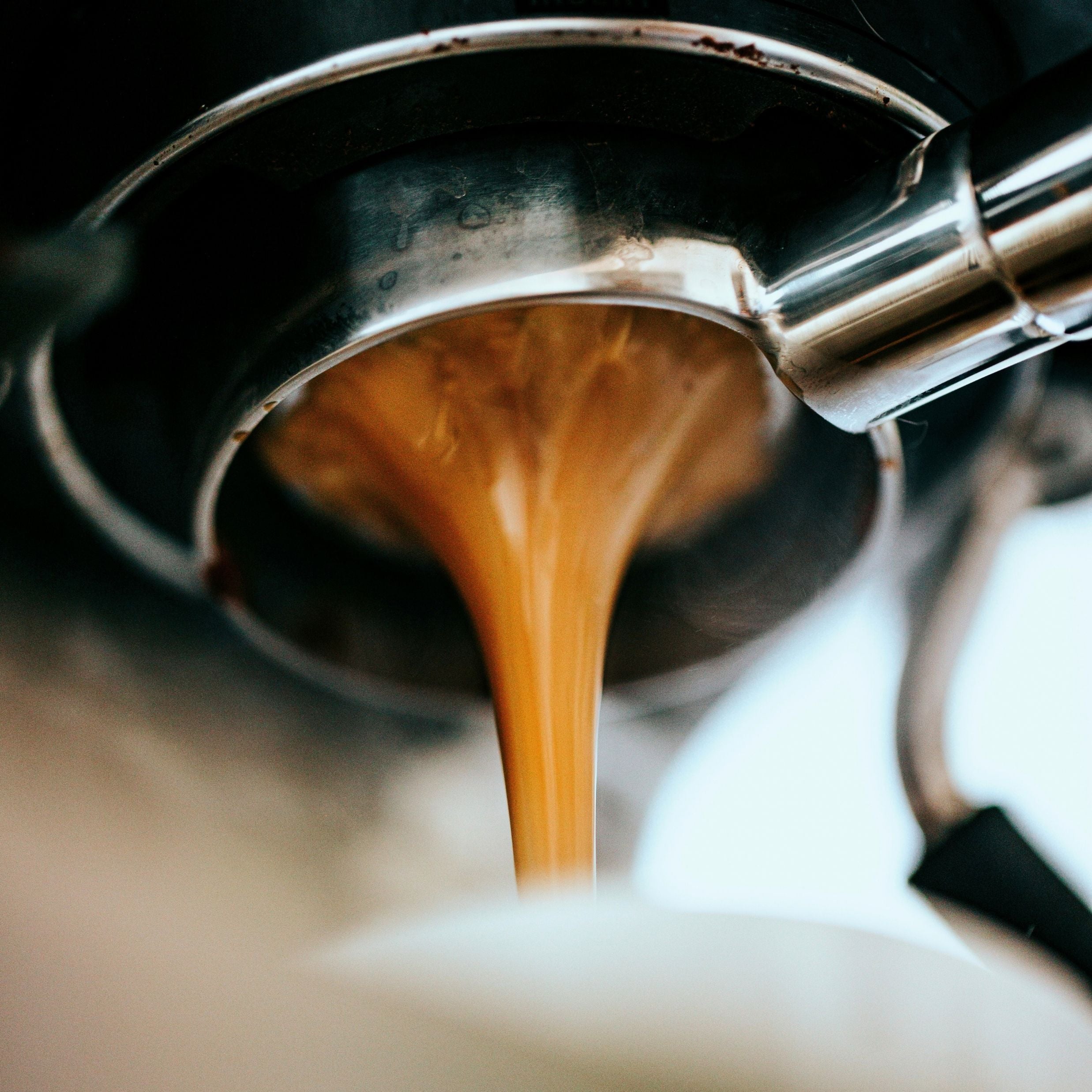 Espresso being poured from a portafilter into a white cup.